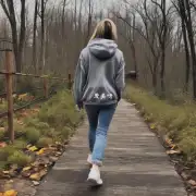 在一座公园的小路上一位穿着灰色连帽卫衣牛仔裤和运动鞋的女性正沿着小径散步吗?她的头发是什么颜色呢?